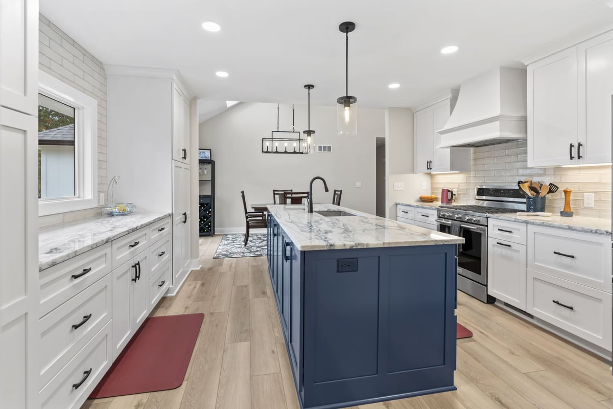 Custom kitchen remodel in Stilwell, KS featuring a blue island, white cabinetry, quartz countertops, new flooring, and modern lighting.