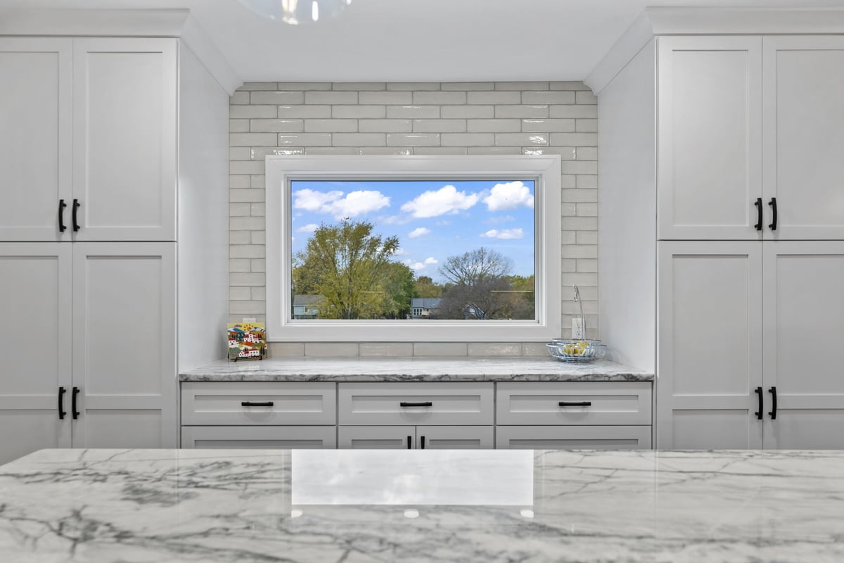 Custom kitchen storage in Stilwell, KS with tall white cabinets, quartz countertops, subway tile backsplash, and large window.