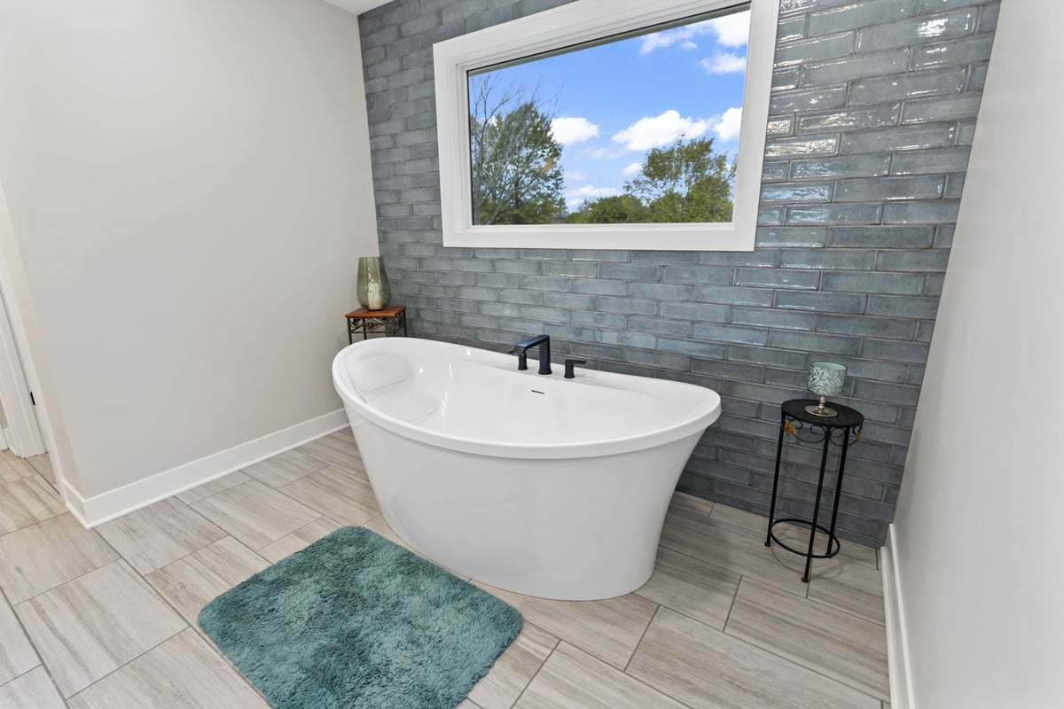 Freestanding soaking tub in Stilwell, KS primary bathroom with blue tile accent wall and natural light.