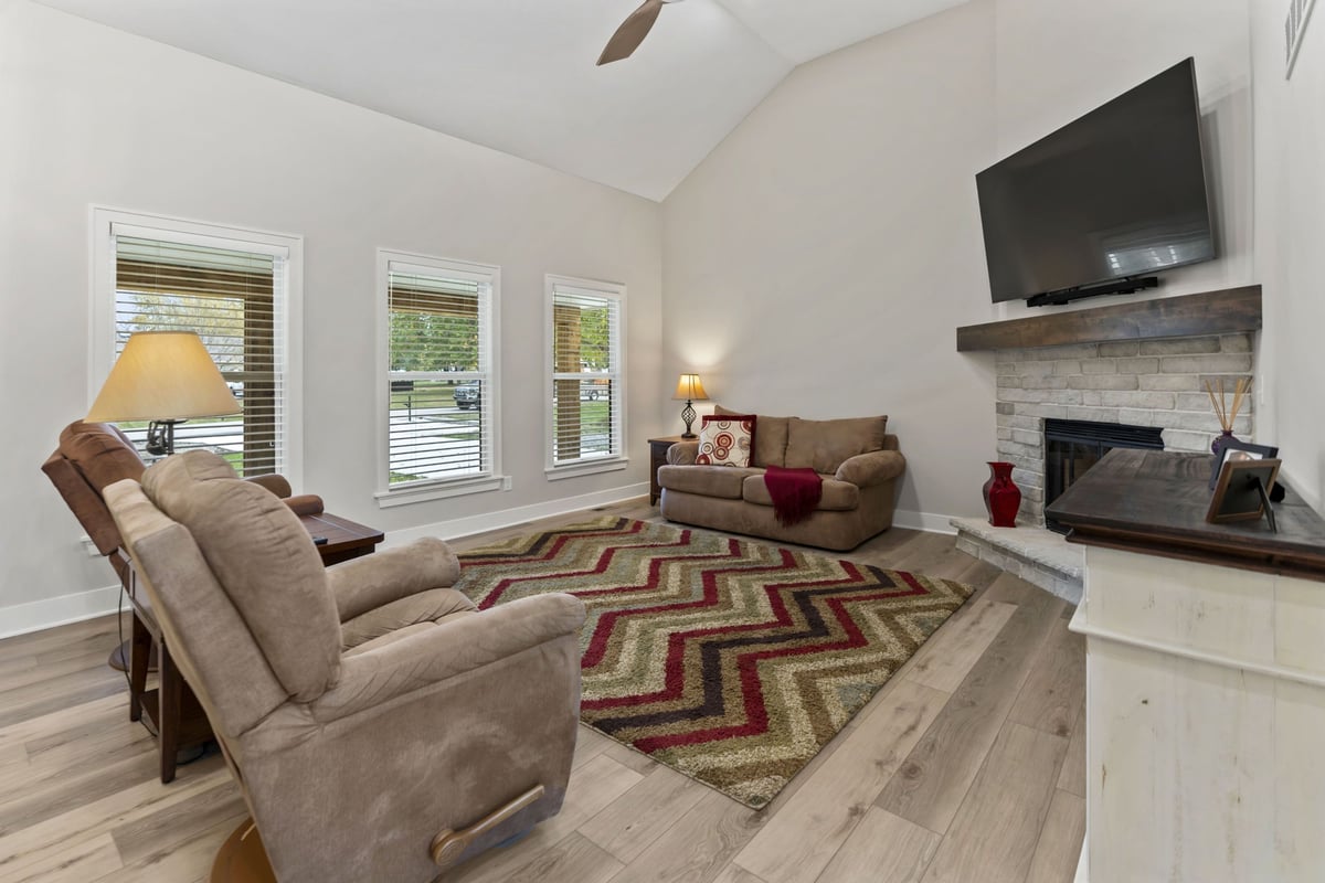 Remodeled living room in Stilwell, KS featuring new floors, updated fireplace surround, large windows, and vaulted ceiling.