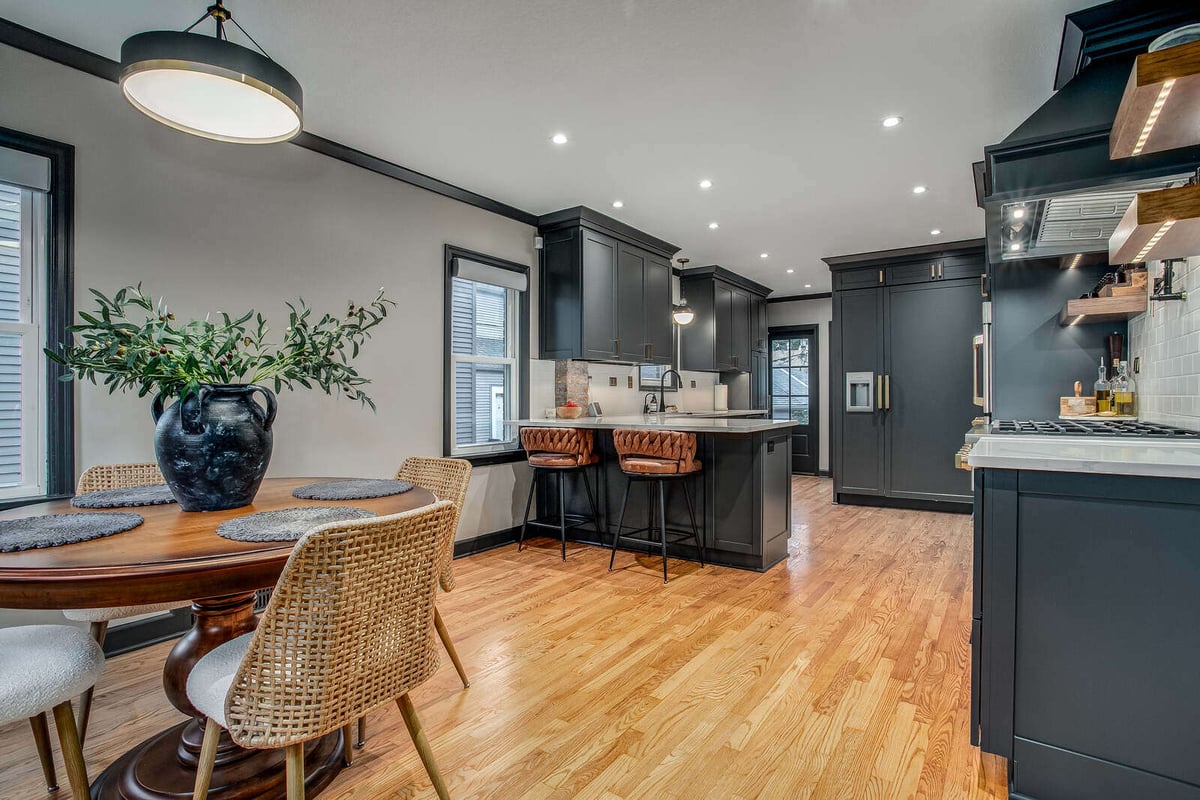 Open-concept kitchen and dining space with black cabinets and warm wood flooring in a Waldo, MO remodel by Top Shelf Home Builders
