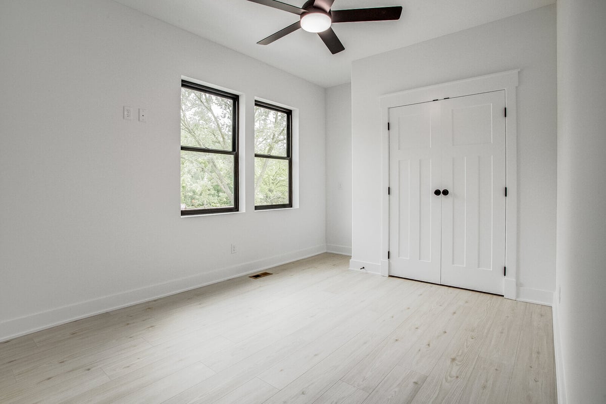 Bright and spacious bedroom with a modern ceiling fan, double doors, and large windows in a Kansas City whole home remodel