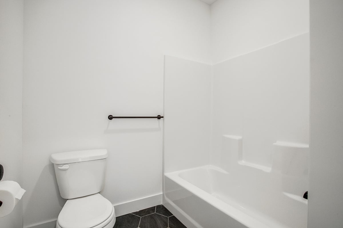Minimalist bathroom with a white tub-shower combo, black towel bar, and modern black tile flooring in a Metro Kansas City home remodel