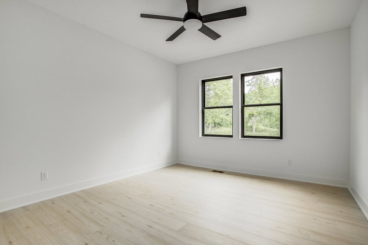 Minimalist bedroom with white walls, black ceiling fan, and large windows in a Kansas City home remodel by Top Shelf Home Builders