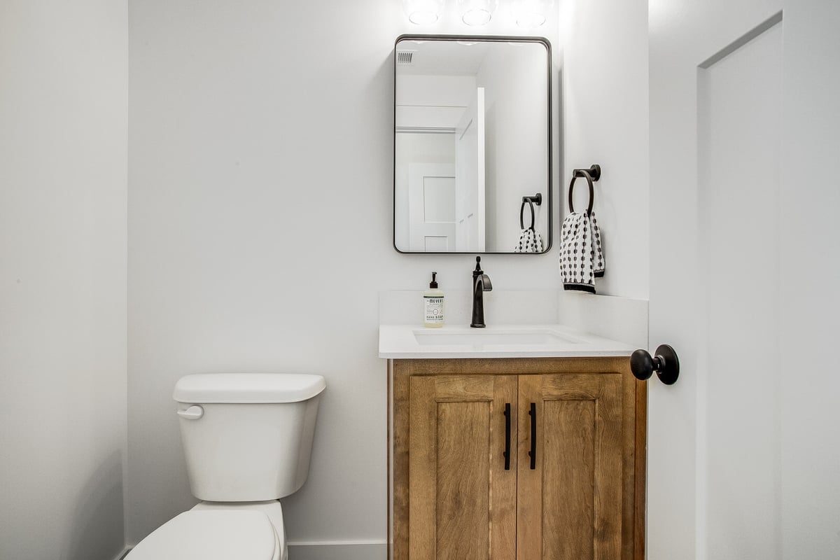 Stylish powder room featuring a wood vanity, black hardware, and a sleek mirror, part of a Metro Kansas City home remodel by Top Shelf Home Builders.jpg