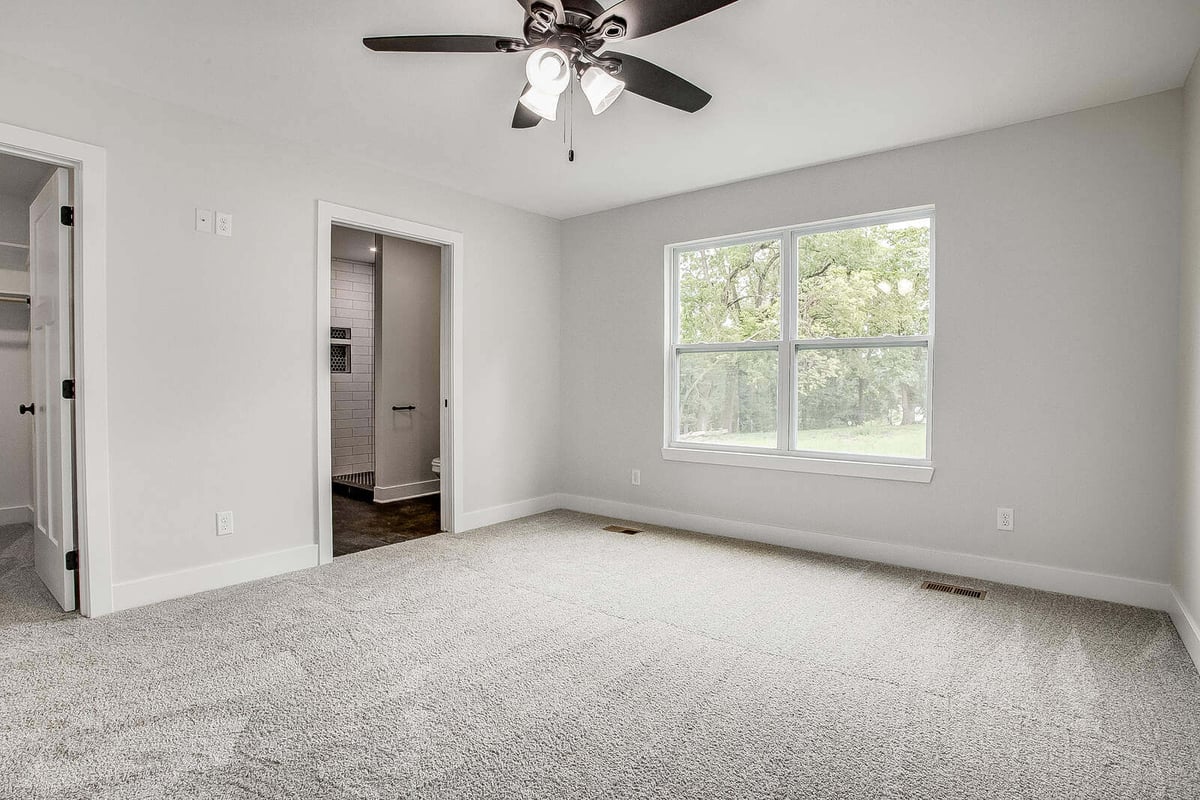 Master bedroom with a ceiling fan, plush carpet, and an en-suite bath in a Metro Kansas City home remodel by Top Shelf Home Builders