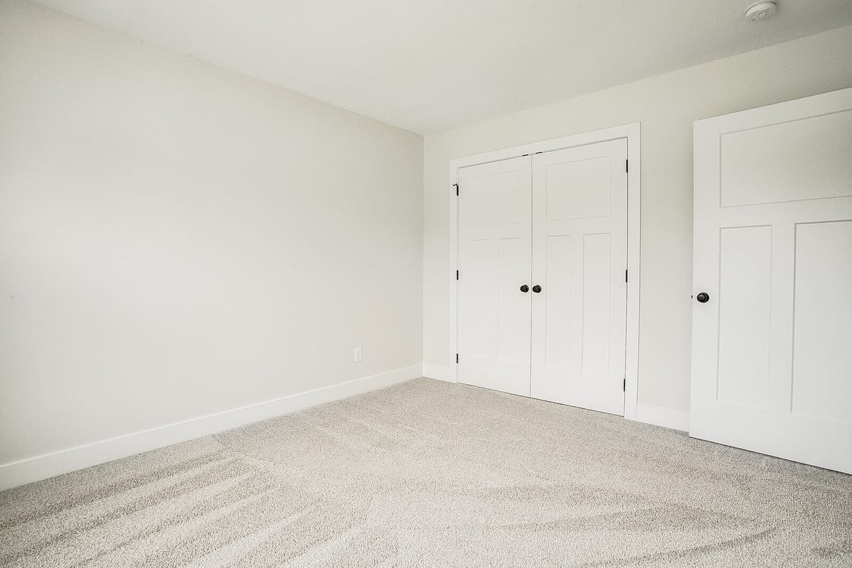 Secondary bedroom with white double-door closet, neutral walls, and plush carpet, part of a Metro Kansas City home remodel by Top Shelf Home Builders.jpg
