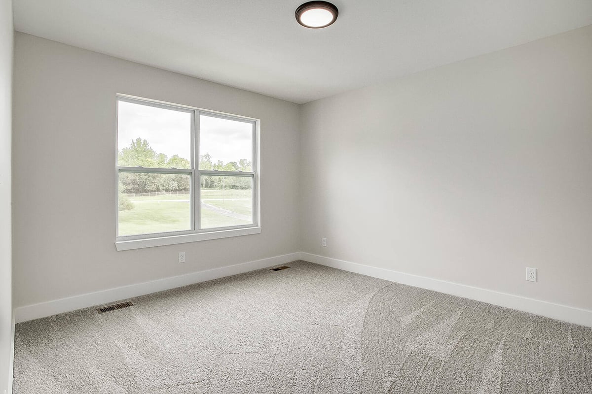 Spacious bedroom with neutral carpeting and a large window overlooking greenery, part of a Metro Kansas City home remodel by Top Shelf Home Builders