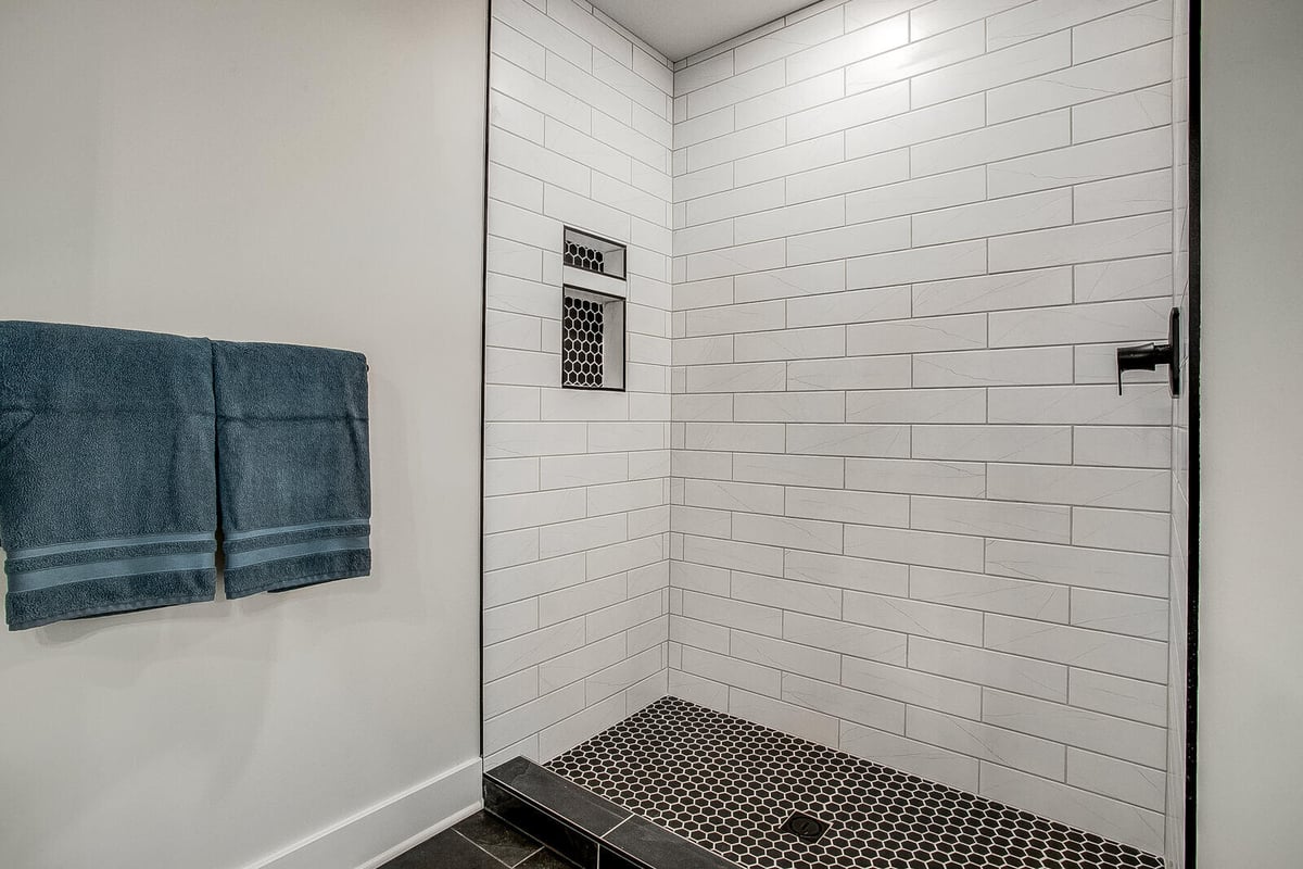 Walk-in shower with white subway tiles and black hexagonal floor tiles, part of a whole home remodel by Top Shelf Home Builders