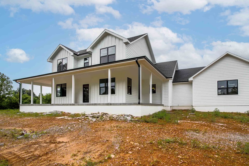 Elegant custom-built farmhouse with a wraparound porch and black window accents, designed by Top Shelf Home Builders in Metro Kansas City
