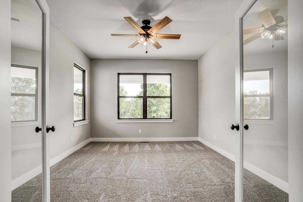 Beautiful bedroom remodel with neutral gray walls, plush carpeting, and a ceiling fan by Top Shelf Home Builders in Metro Kansas City