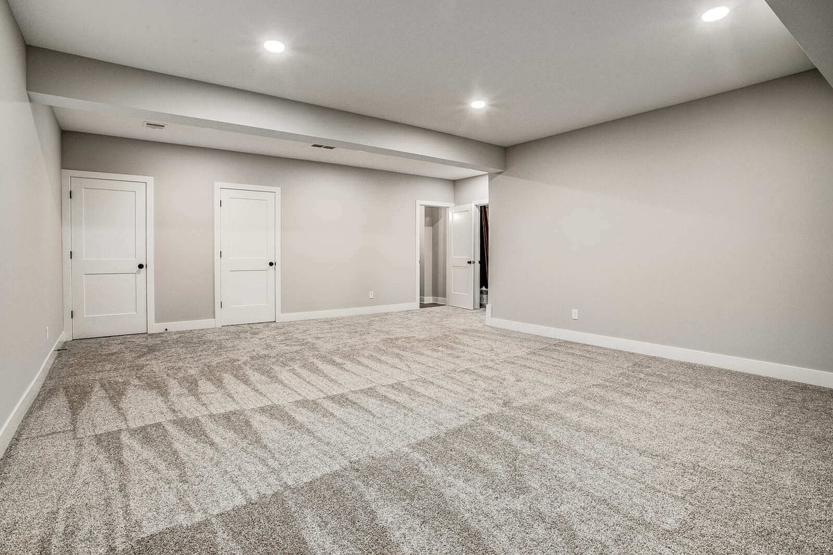 Fully renovated basement with neutral carpeting, recessed lighting, and additional storage space by Top Shelf Home Builders