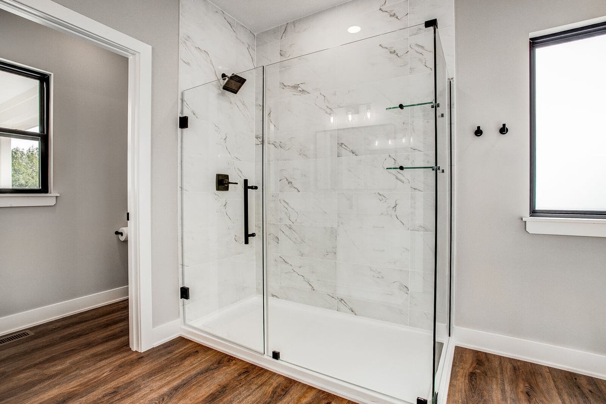 Modern glass-enclosed shower with marble tile walls and black fixtures, part of a Kansas City home remodel by Top Shelf Home Builders