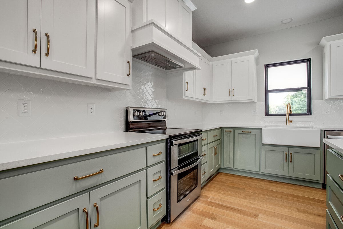 Modern kitchen remodel with green lower cabinets, white upper cabinets, and gold hardware by Top Shelf Home Builders in Metro Kansas City