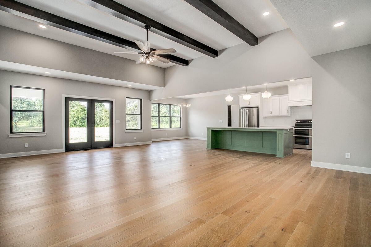 Open-concept living area with a vaulted ceiling, dark wood beams, and a green kitchen island, remodeled by Top Shelf Home Builders in Kansas City.jpg