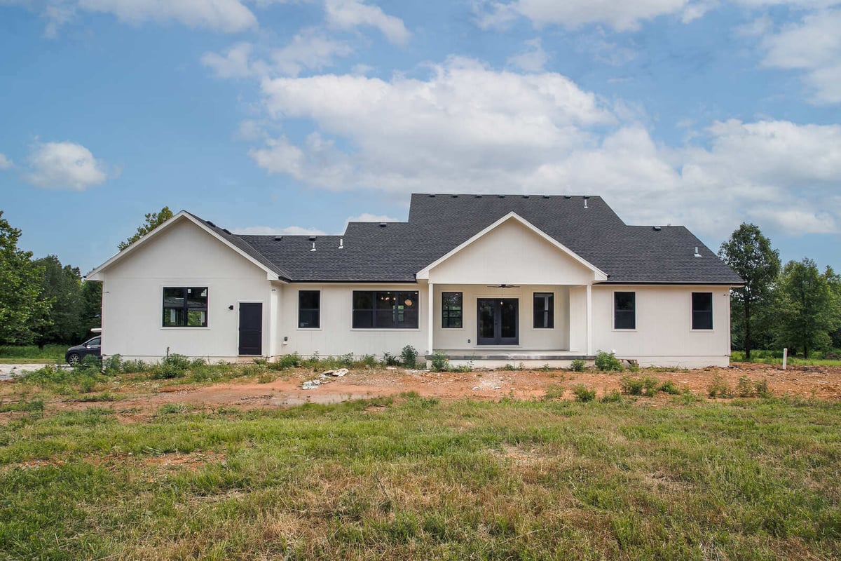 Rear view of a modern farmhouse with a black roof, white siding, and an extended covered patio, completed by Top Shelf Home Builders
