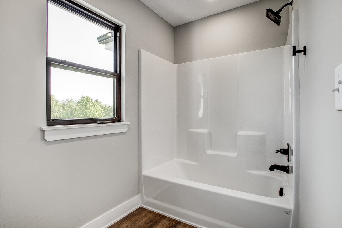 Renovated bathroom with a white bathtub, black fixtures, and a large window, completed by Top Shelf Home Builders in Kansas City