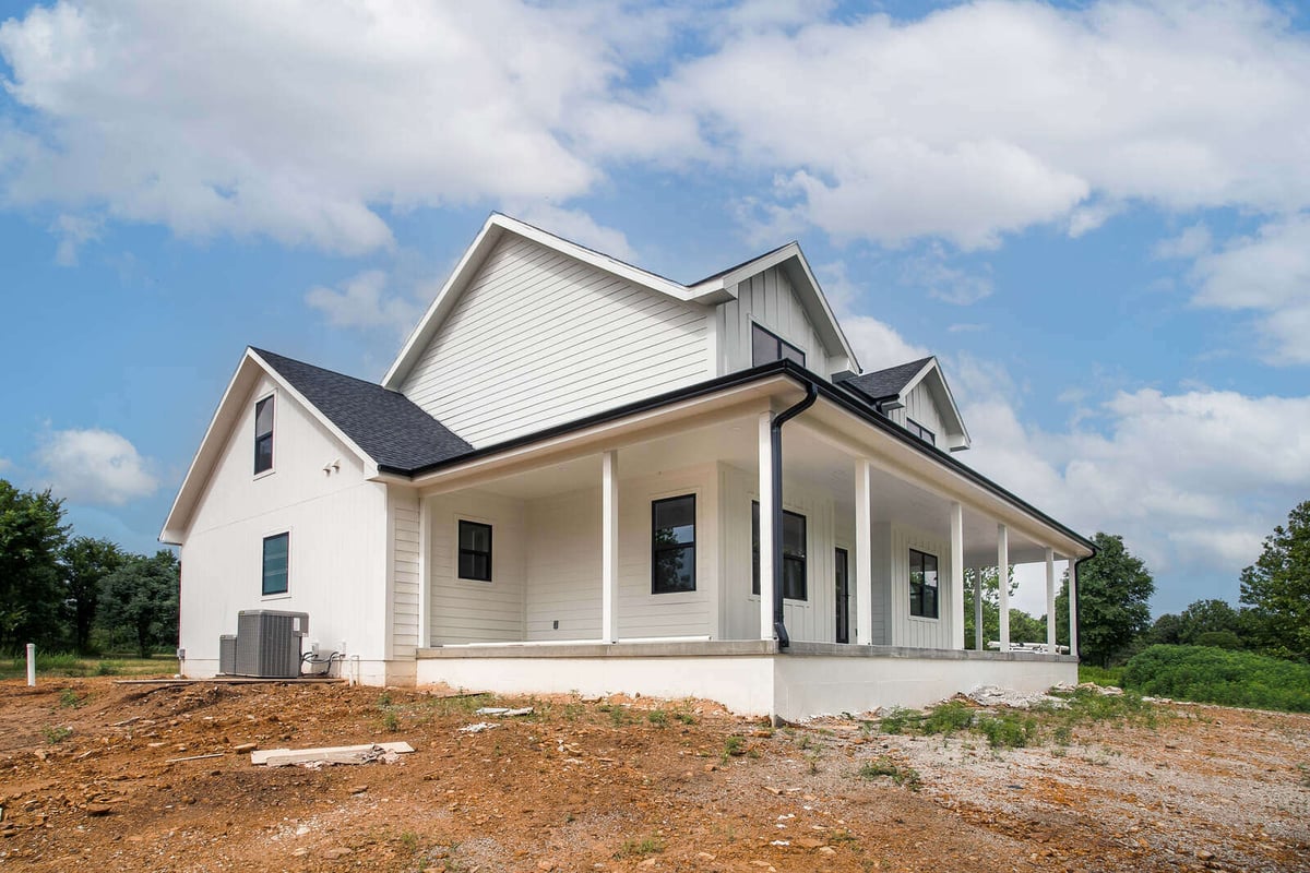 Side view of a newly built farmhouse with black trim, a wraparound porch, and a steep roofline by Top Shelf Home Builders in Metro Kansas City