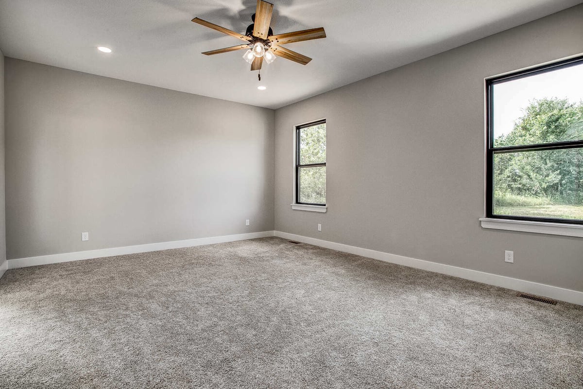 Spacious remodeled bedroom with neutral gray walls and a modern ceiling fan in a Kansas City home by Top Shelf Home Builders