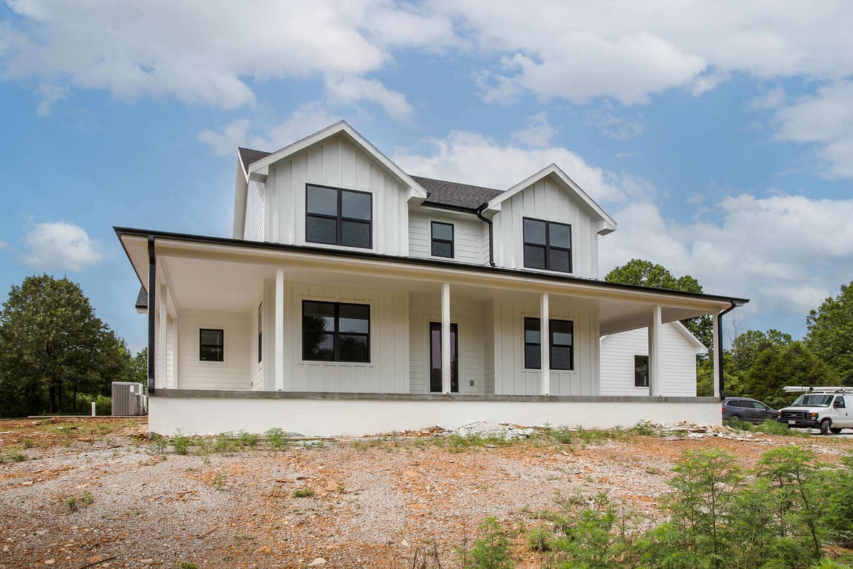 Stunning front view of a modern farmhouse with double gable rooflines, a covered porch, and black-trimmed windows
