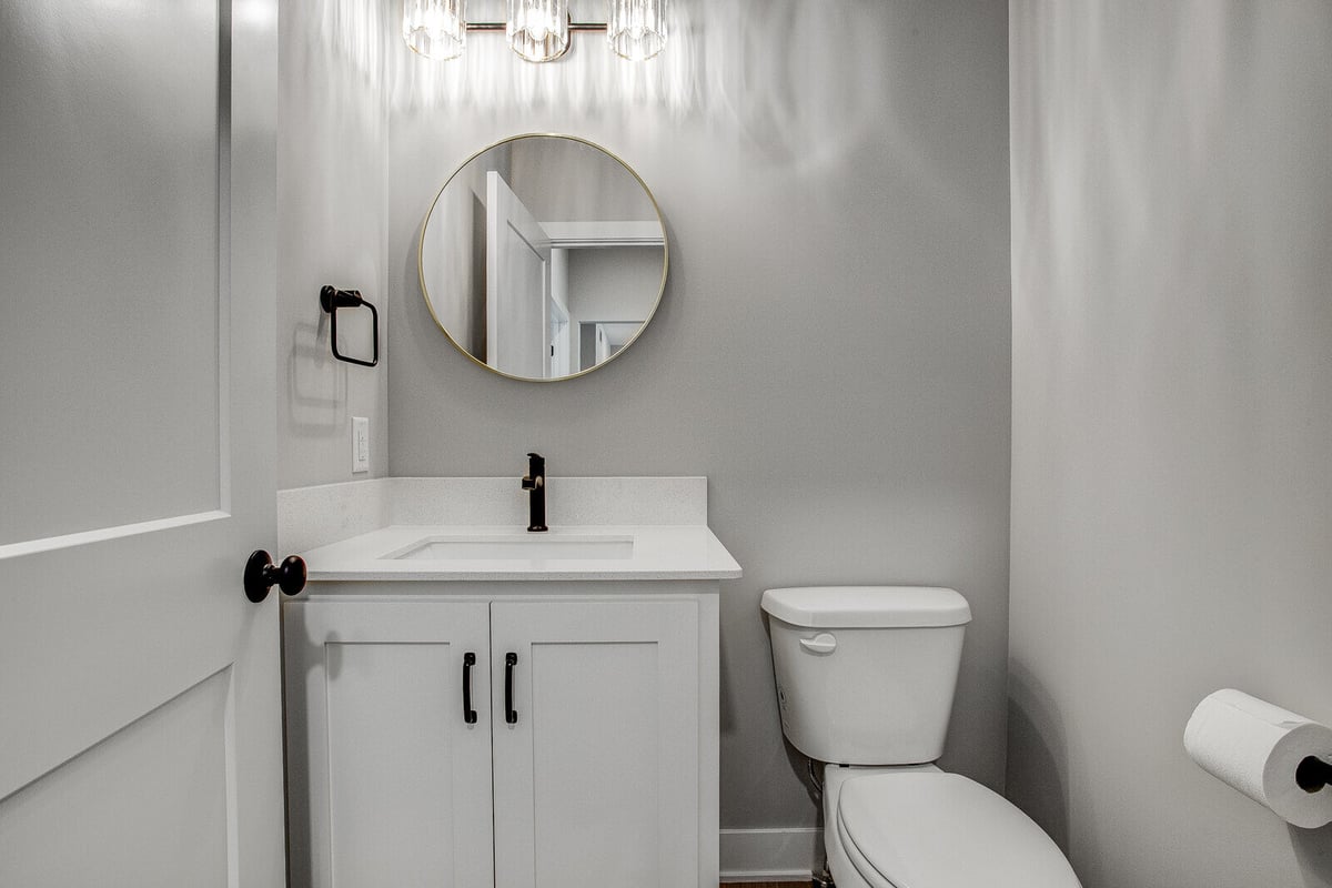 Stylish half-bathroom with a round mirror, gold accents, and black fixtures, remodeled by Top Shelf Home Builders in Kansas City
