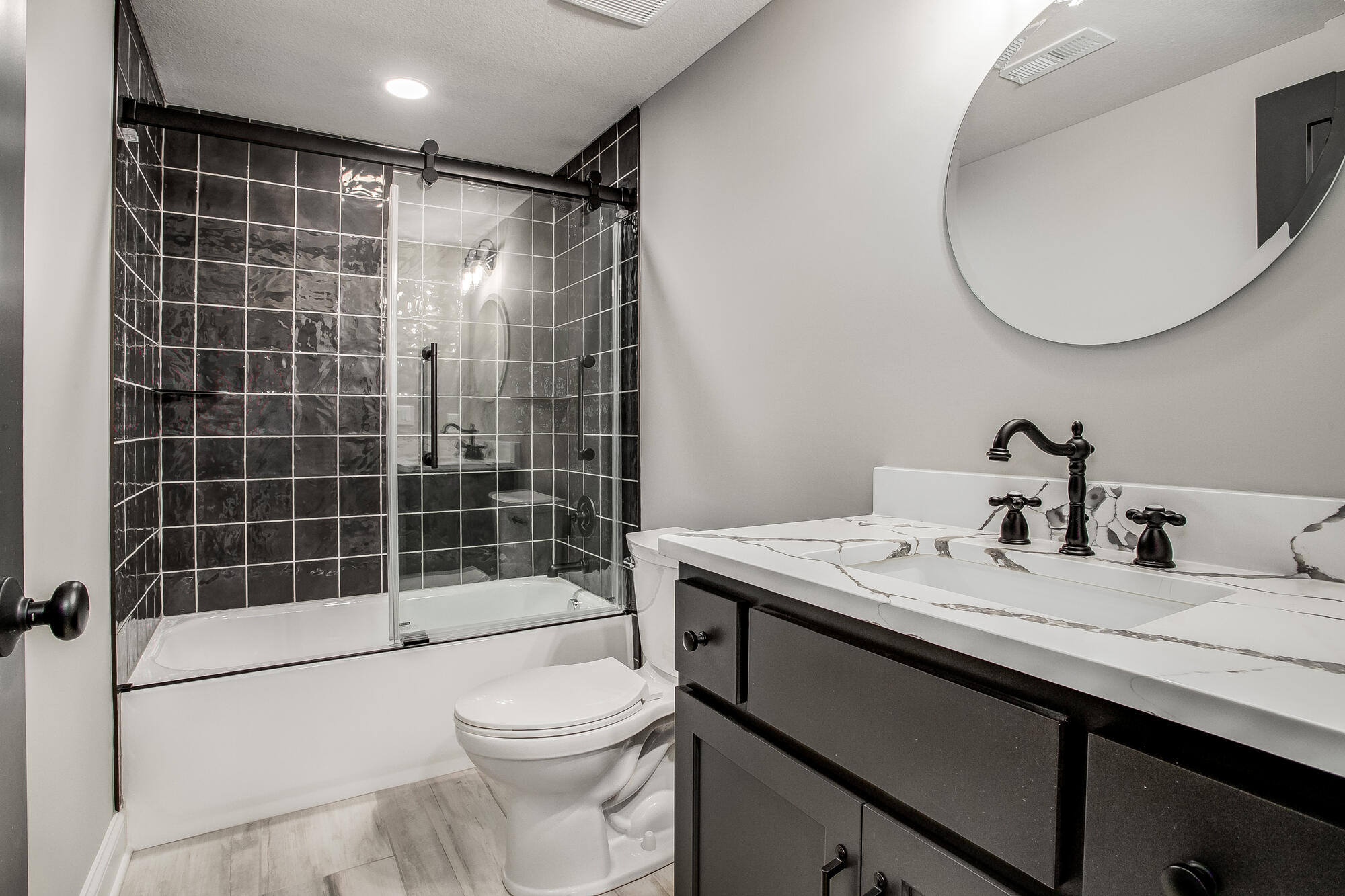 Modern bathroom with a black tile shower, sliding glass door, and a white vanity in a Metro Kansas City home remodel