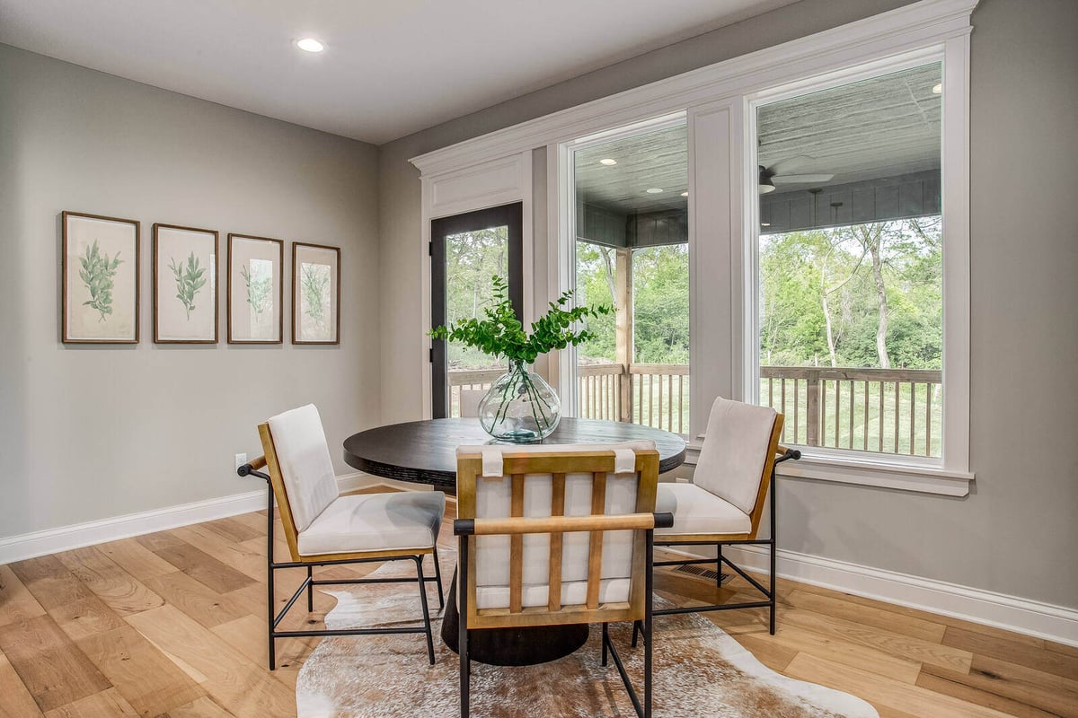 Cozy dining nook with a round black table, upholstered chairs, and large windows overlooking a covered porch in Metro Kansas City