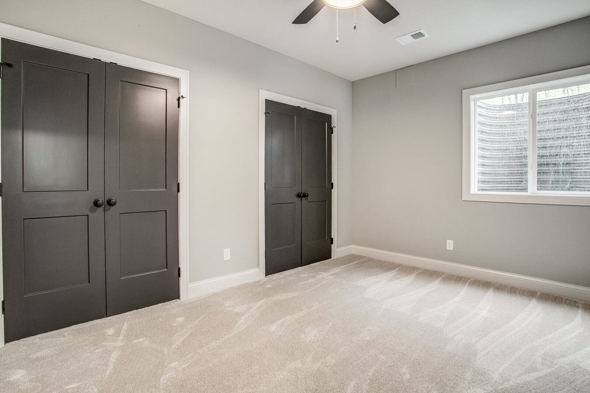 Cozy guest bedroom with neutral carpet, natural light, and stylish black doors in a Kansas City home remodel