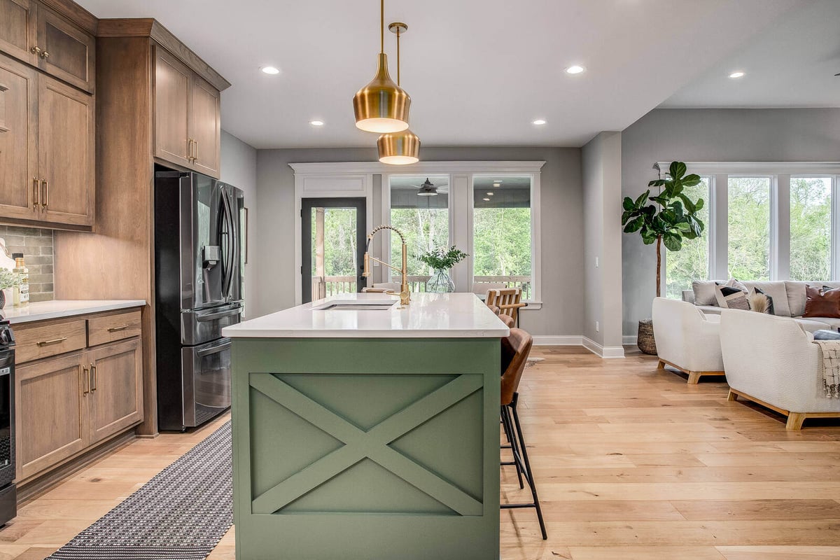 Open-concept kitchen and living area featuring a large green island, gold pendant lights, and a modern aesthetic