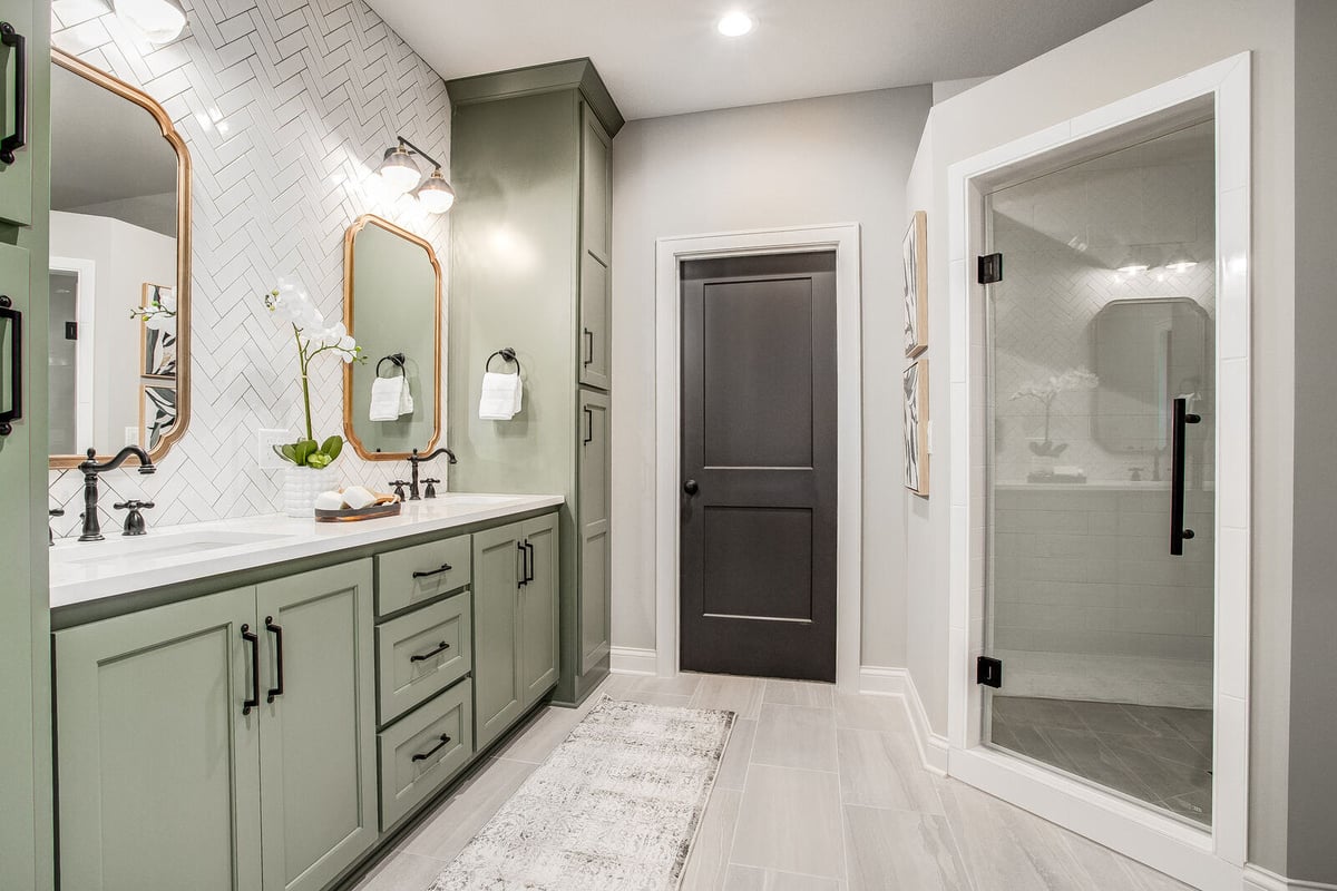 Stunning bathroom with sage green cabinetry, gold accents, and a double vanity in a Metro Kansas City home remodel